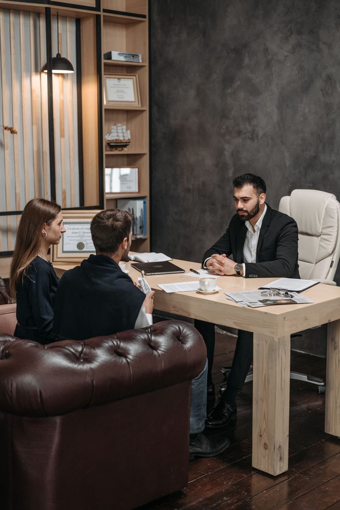 A professional business meeting with three people discussing documents in an office setting.